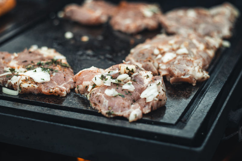 Man uses a steel ladle to turn a loaded pork neck with basil, salt, pepper and oil 