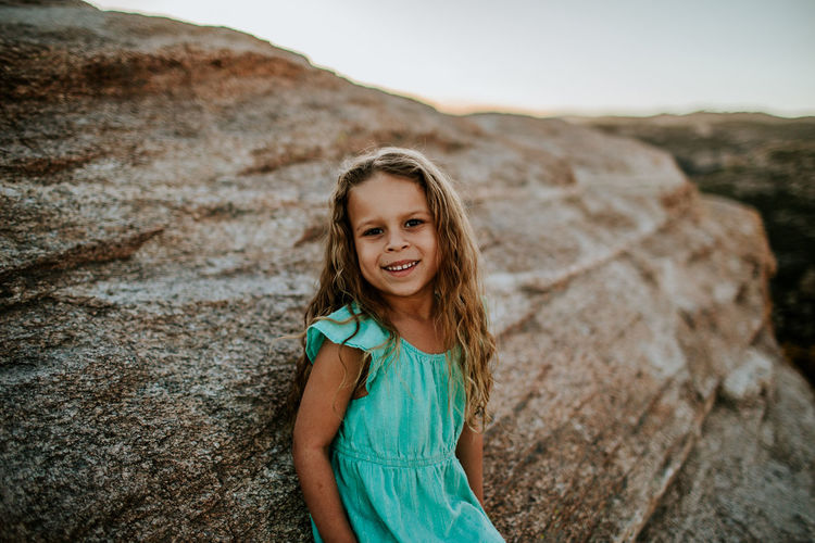 Young girl leaning against large rock