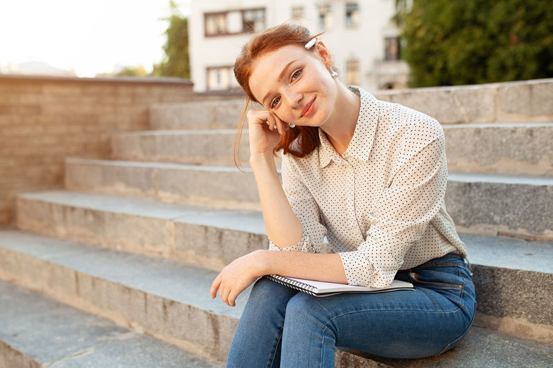Woman holding book while sitting on steps