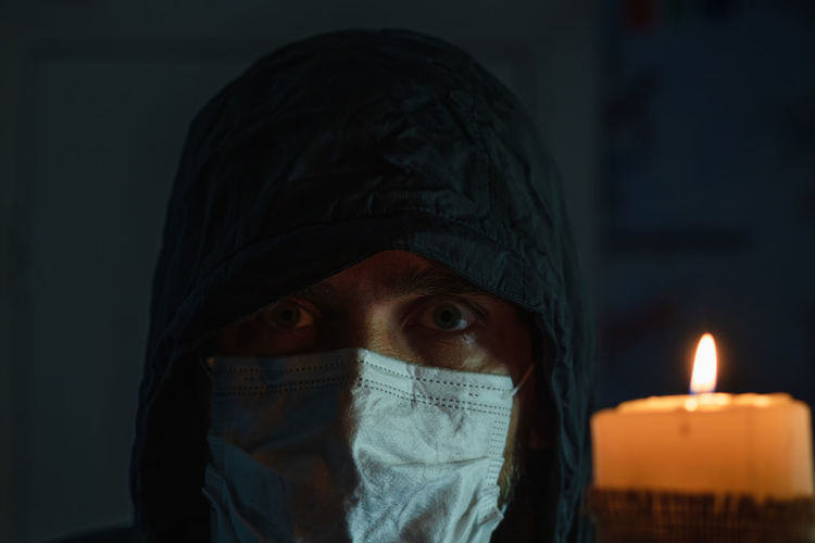Close-up of the face of a man wearing a black hood and medical mask against the background