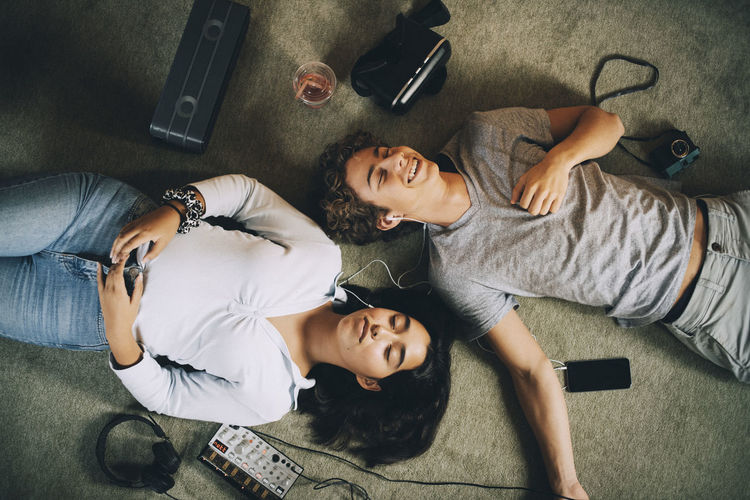 Directly above shot of smiling friends listening music while resting together on carpet at home