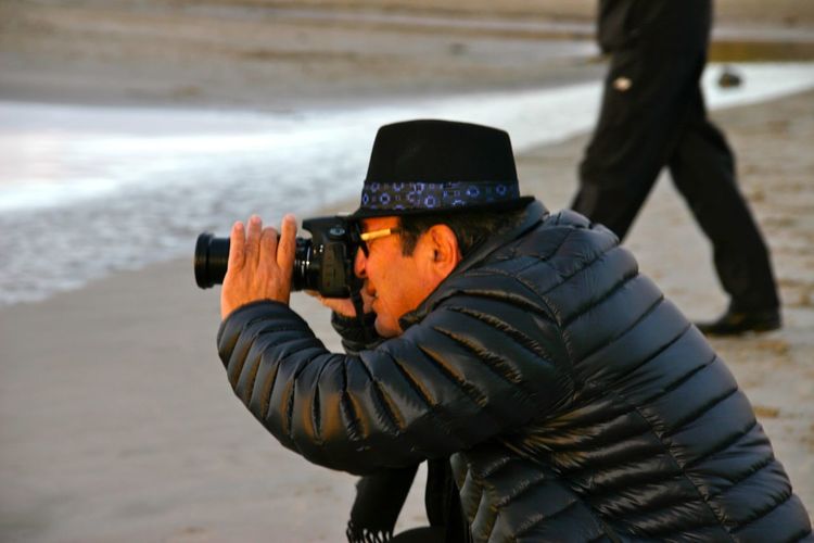 Side view of man photographing with camera at beach