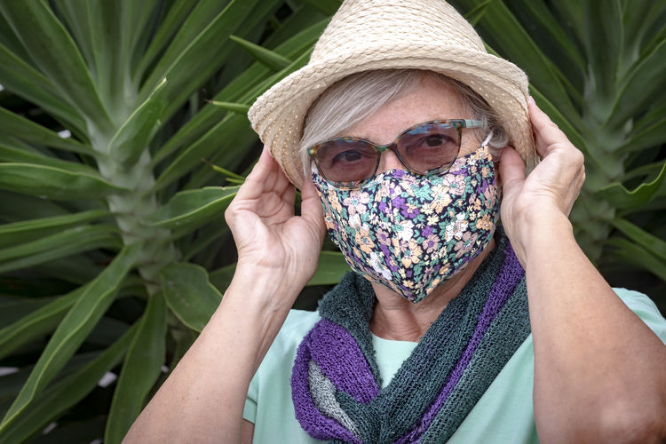 Portrait of senior woman wearing hat standing against plants