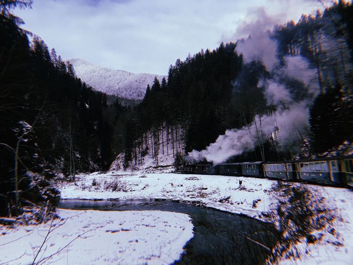 Train passing by snow by trees on covered mountains against sky
