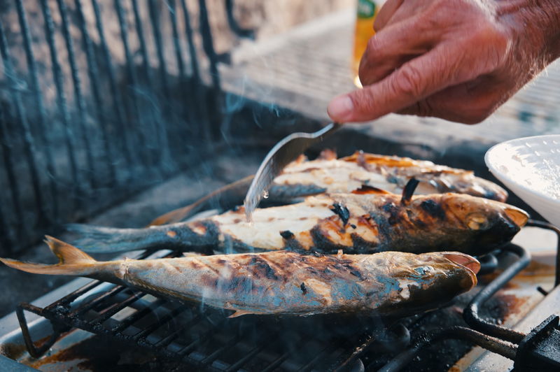 Cropped hand of man preparing food on barbecue grill