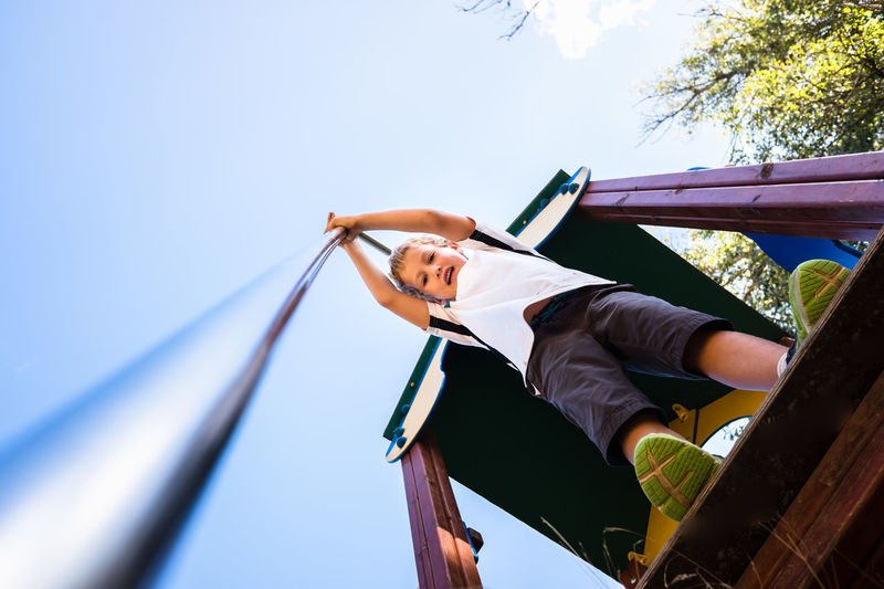 Low angle view of boy standing on slide at playground against sky