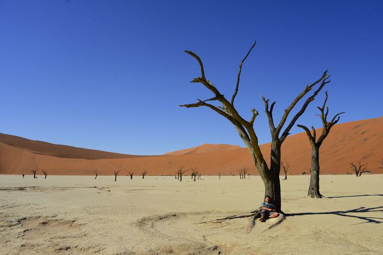 Man relaxing on desert against clear blue sky