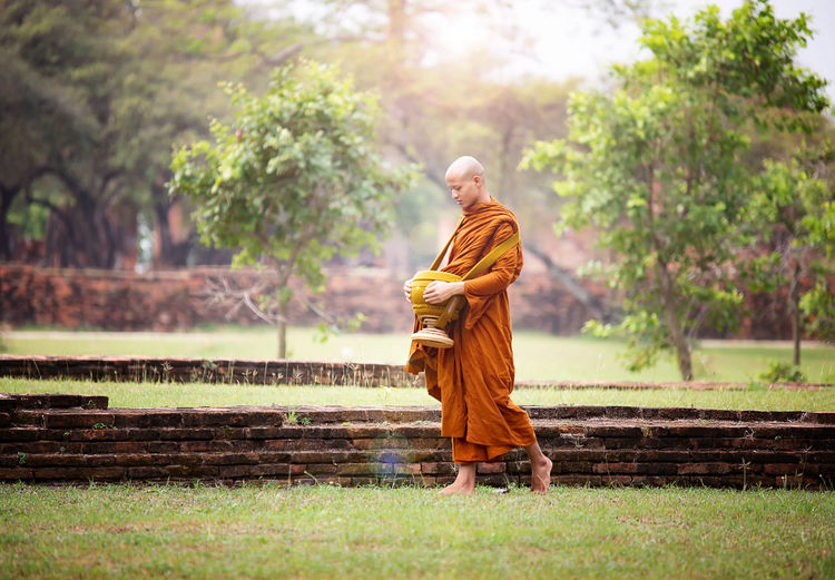 Full length of monk walking with urn on grass
