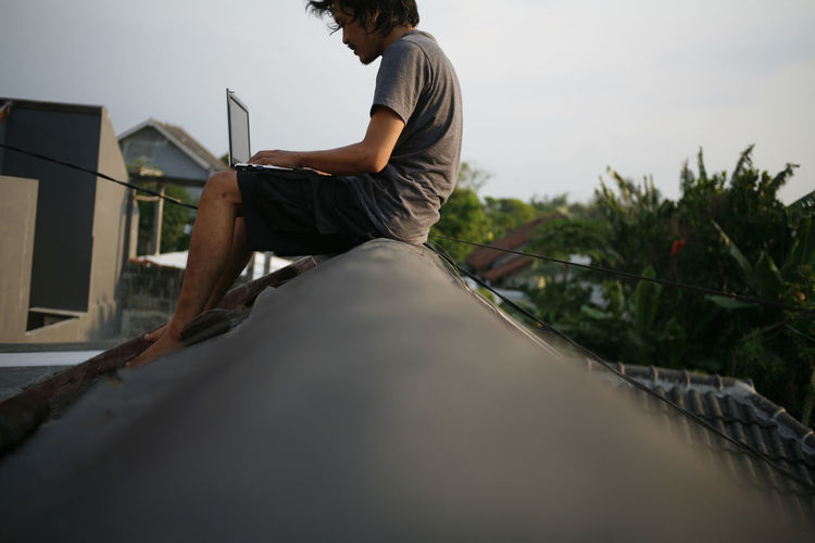Side view of man sitting and working on rooftop