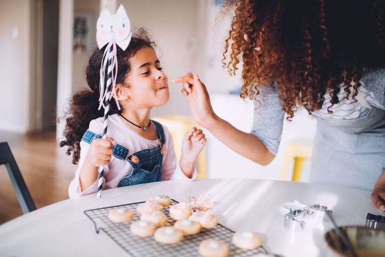 Mother feeding cookies to daughter at home