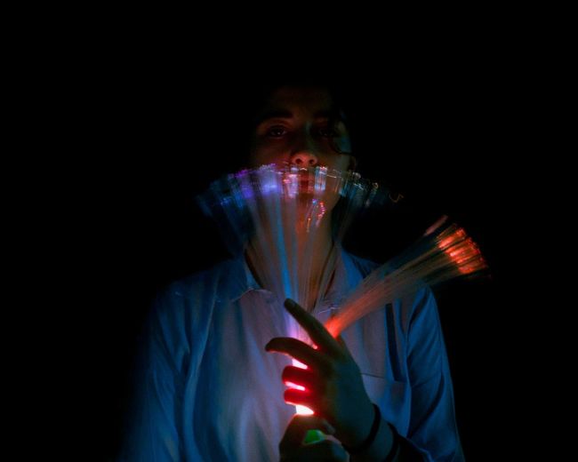 Portrait of woman holding illuminated lighting equipment against black background