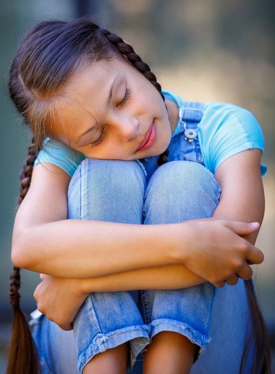 Close-up of girl hugging knees outdoors