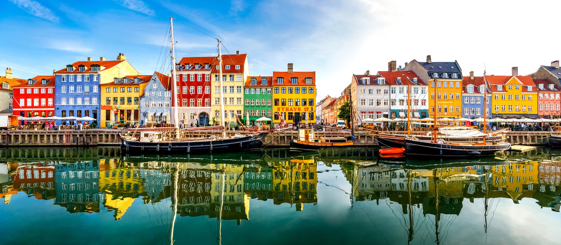 Sailboats moored in river by buildings against sky