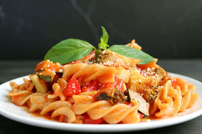 Closeup of delectable wholemeal fusilli pasta in tomato sauce served on black backdrop