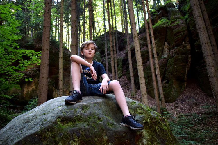 Full length of boy sitting on swing in forest