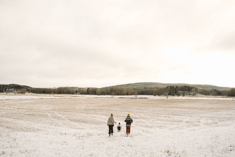 Lesbian mothers and daughter running on snow covered land
