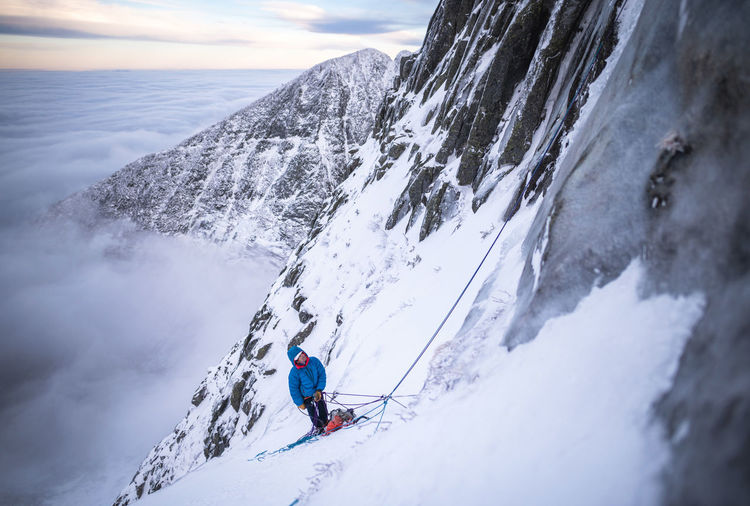 A male climber belaying his lead during a cold winter alpine climb