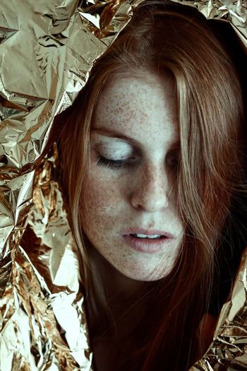 Close-up young woman with freckles on face covered in silver foil