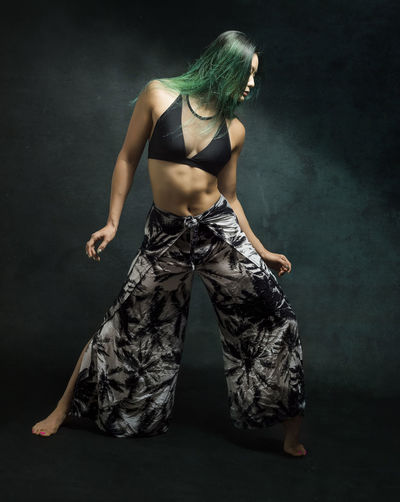 Full length of sensuous female dancer with green dyed hair against wall