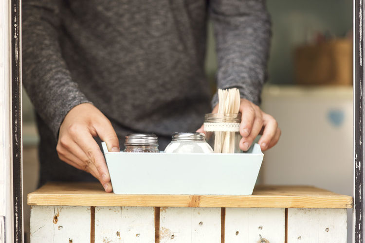 Midsection of male owner placing salt and pepper shakers with forks in container at food truck window