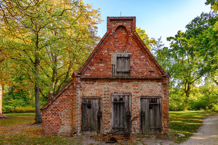Small rough old brick house and wooden dirty doors and windows located in rural area in autumn.