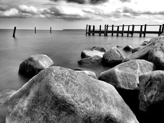 Rocks on shore by pier against sky
