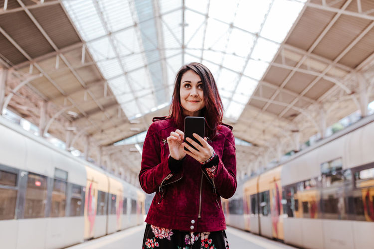 Smiling woman using mobile phone while standing at railroad station platform