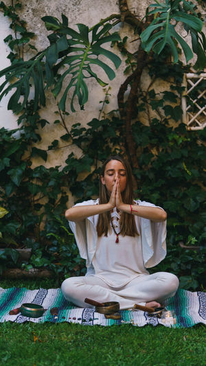 Full length of young woman meditating while sitting outdoors