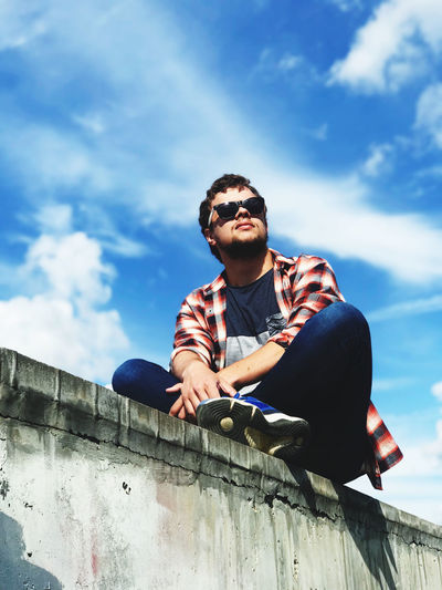 Low angle view of young man sitting on wall