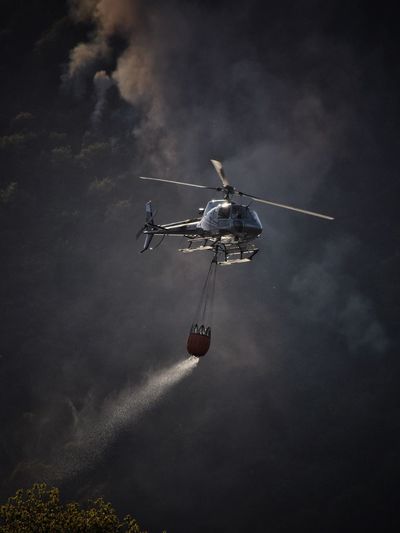 Low angle view of helicopter flying in sky fighting forest fire