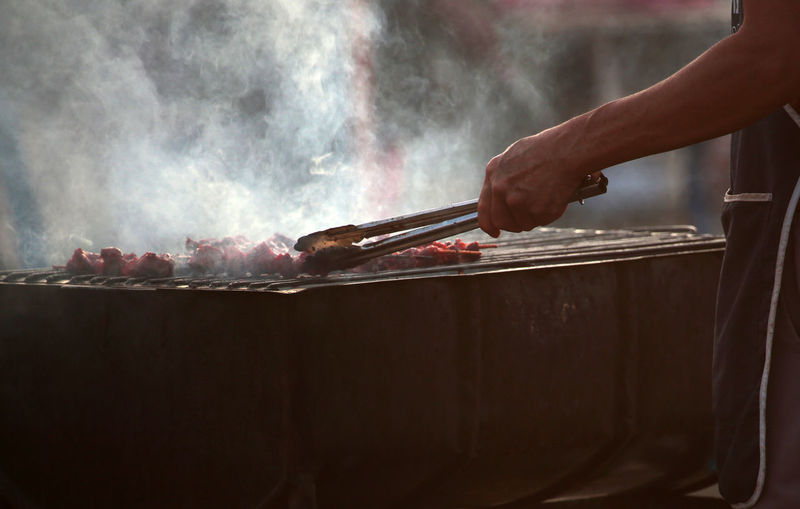 Man with serving tong preparing food on barbecue grill