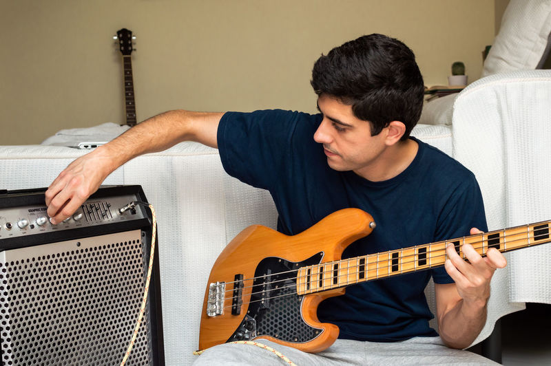 Man adjusting amplifier to play electric bass sitting at home.