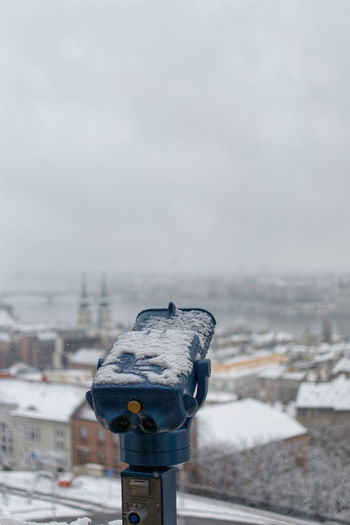 Close-up of coin-operated binoculars against cityscape during winter