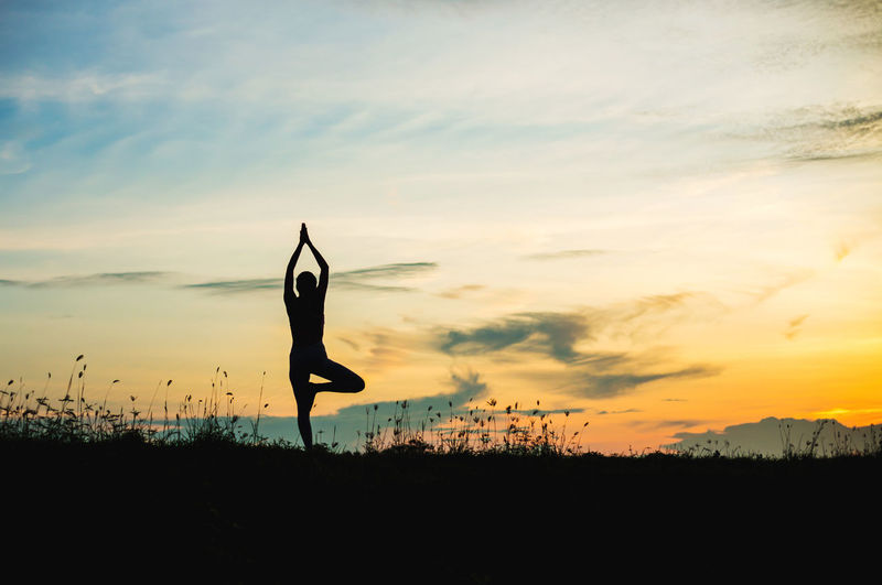 Silhouette woman practicing yoga on land against sky during sunset