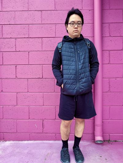 Portrait of young asian man in eyeglasses standing in front of pink brick wall.
