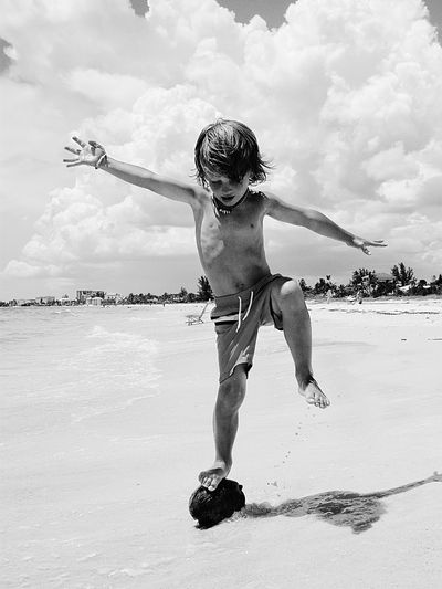 Full length of shirtless boy playing on beach against sky