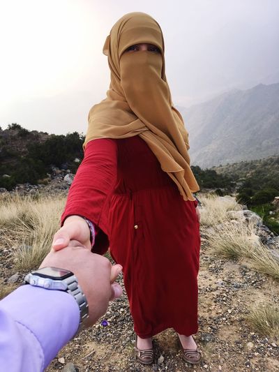 Cropped hand of man holding woman on mountain against sky