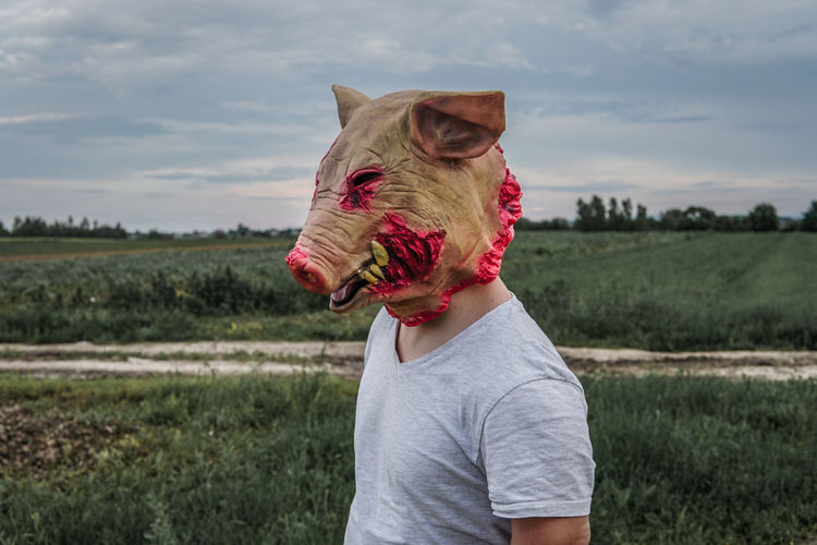 Side view of mid adult man wearing mask standing on land against sky