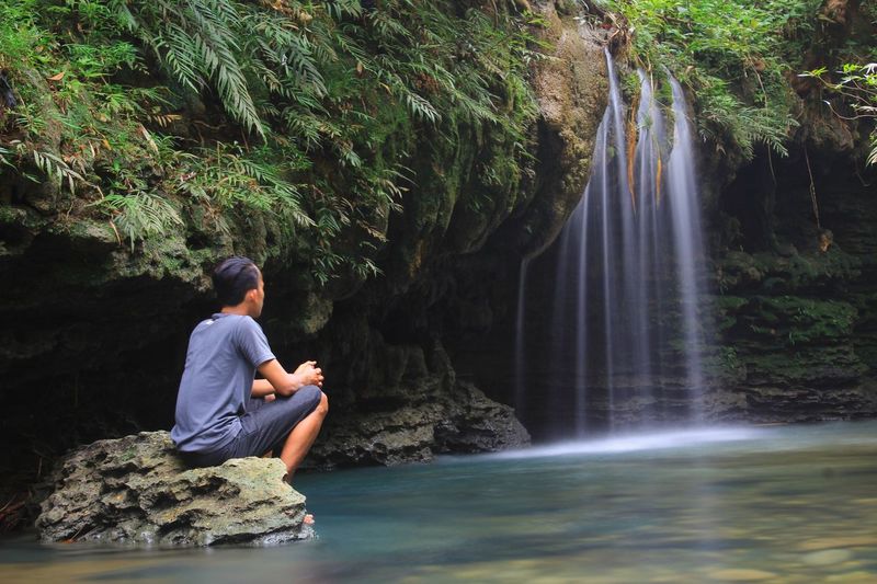 Man sitting on rock against waterfall in forest