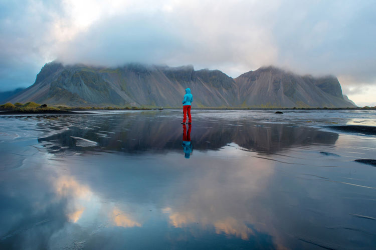 Reflection of a trekking woman and of the vestrahorn mountain in the atlantic ocean, hofn, iceland