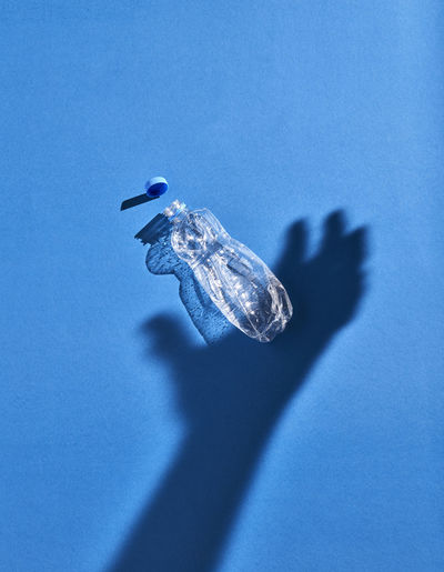 Shadow of a hand and plastic bottle, blue background
