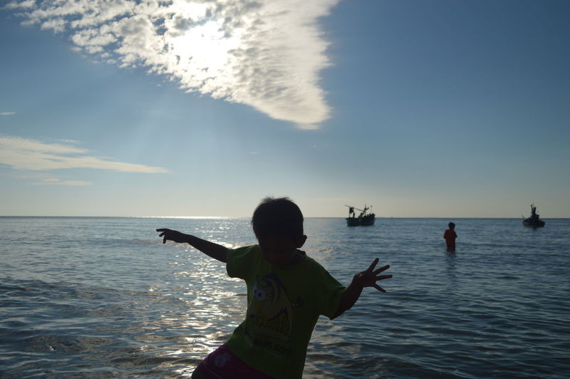Boy playing at beach against sky during sunset