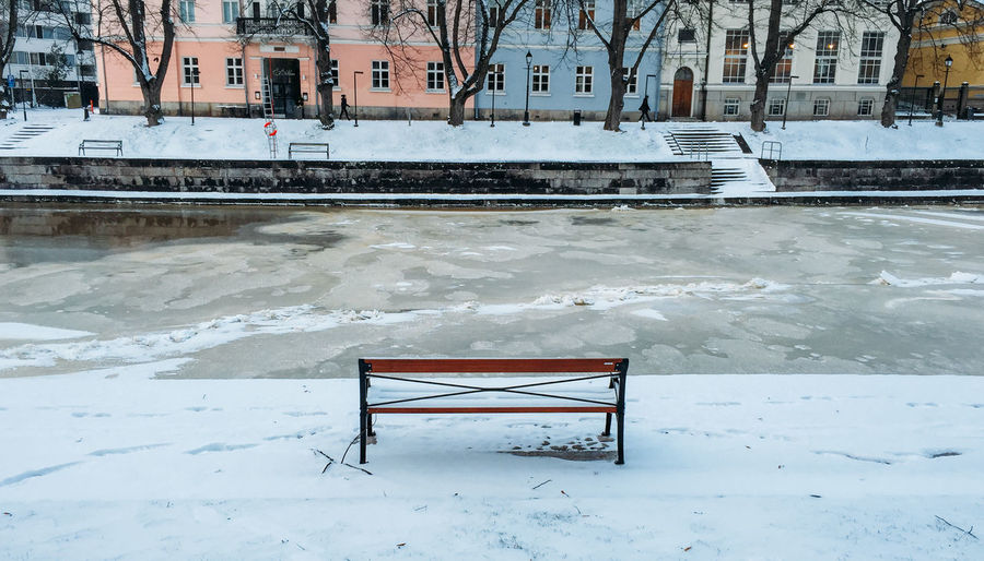 Empty bench on snow against frozen canal