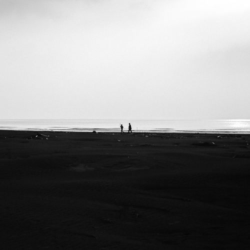 Silhouette people on beach against clear sky