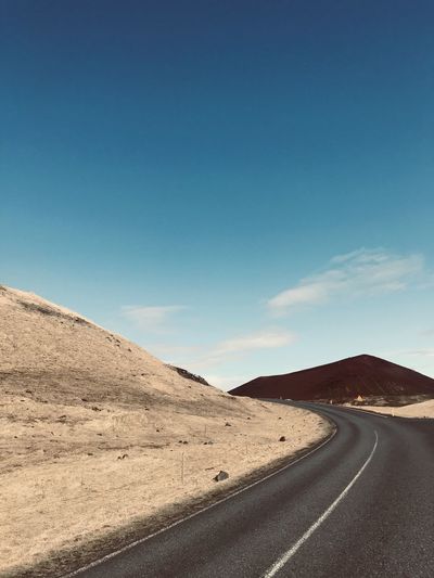 Empty road by desert against blue sky