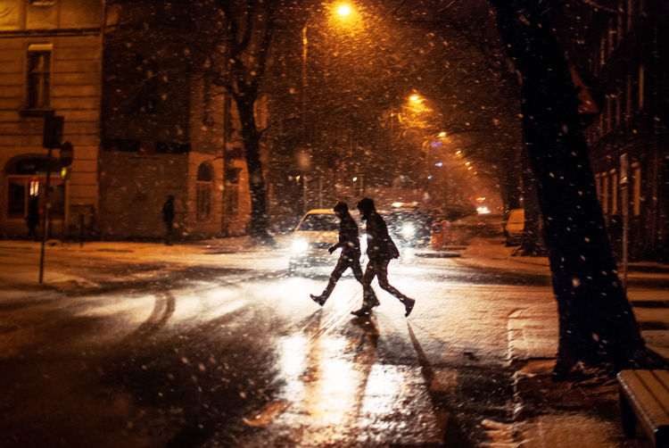 People crossing road during snowfall in city at night