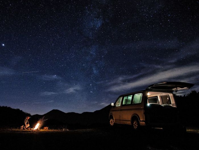 Man with campfire and van on field against star field