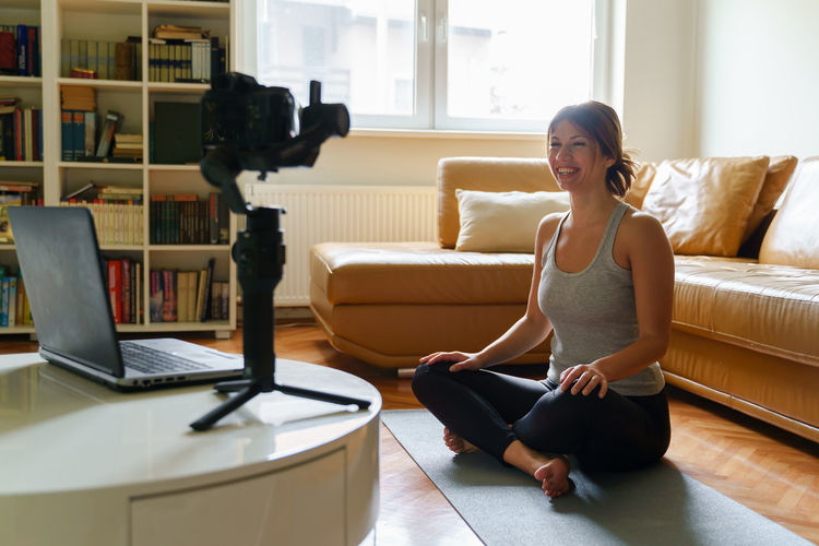 Smiling woman filming while sitting on mat at home