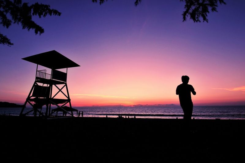 Silhouette man standing against sea during sunset