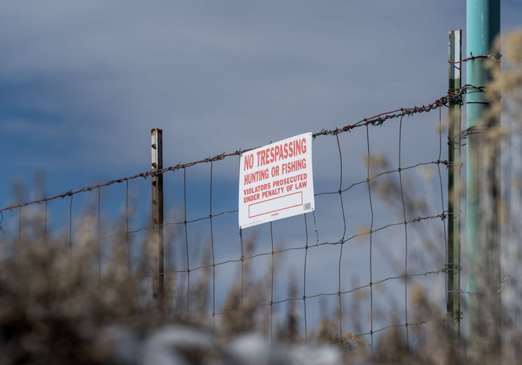 Low angle view of no trespassing sign on fence against sky